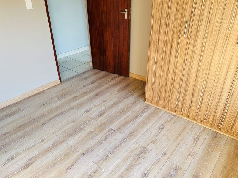 A clean, empty bedroom featuring modern laminate flooring and a built-in wooden wardrobe with a neutral wall finish.