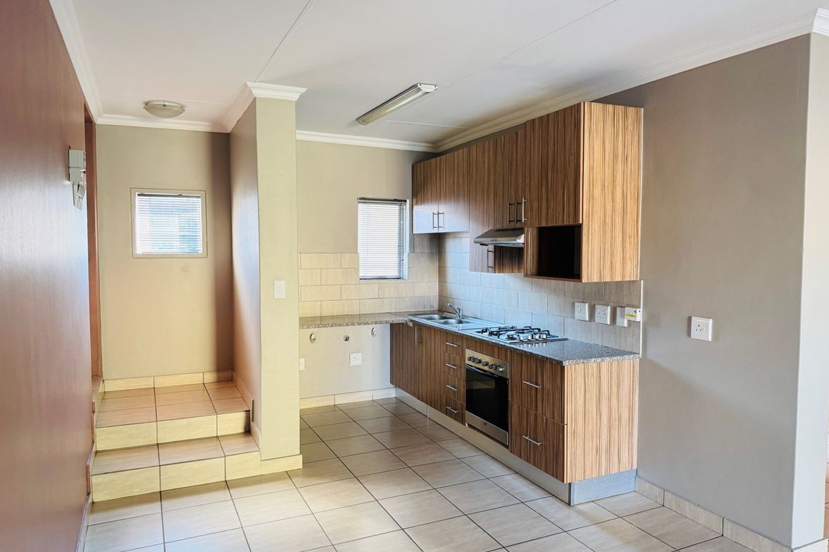 A clean, functional kitchen featuring wood-finish cabinetry, granite countertops, built-in oven and hob, and tiled flooring in an open-plan layout.