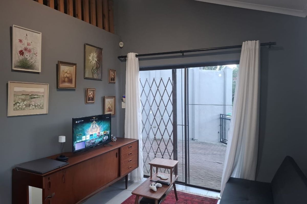 A cozy living room featuring a vaulted ceiling, timber slat detailing, and a sliding glass door with a security gate leading to an outdoor area.