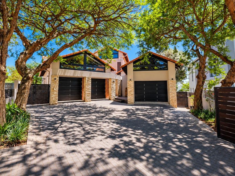 A well-maintained front exterior featuring a triple garage with stone cladding, paved driveway, and mature trees providing shade.
