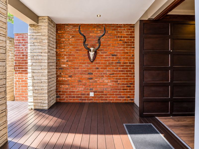 A welcoming entrance area featuring a striking exposed brick feature wall, stone-clad pillar, and high-quality timber decking leading to a solid wood front door.