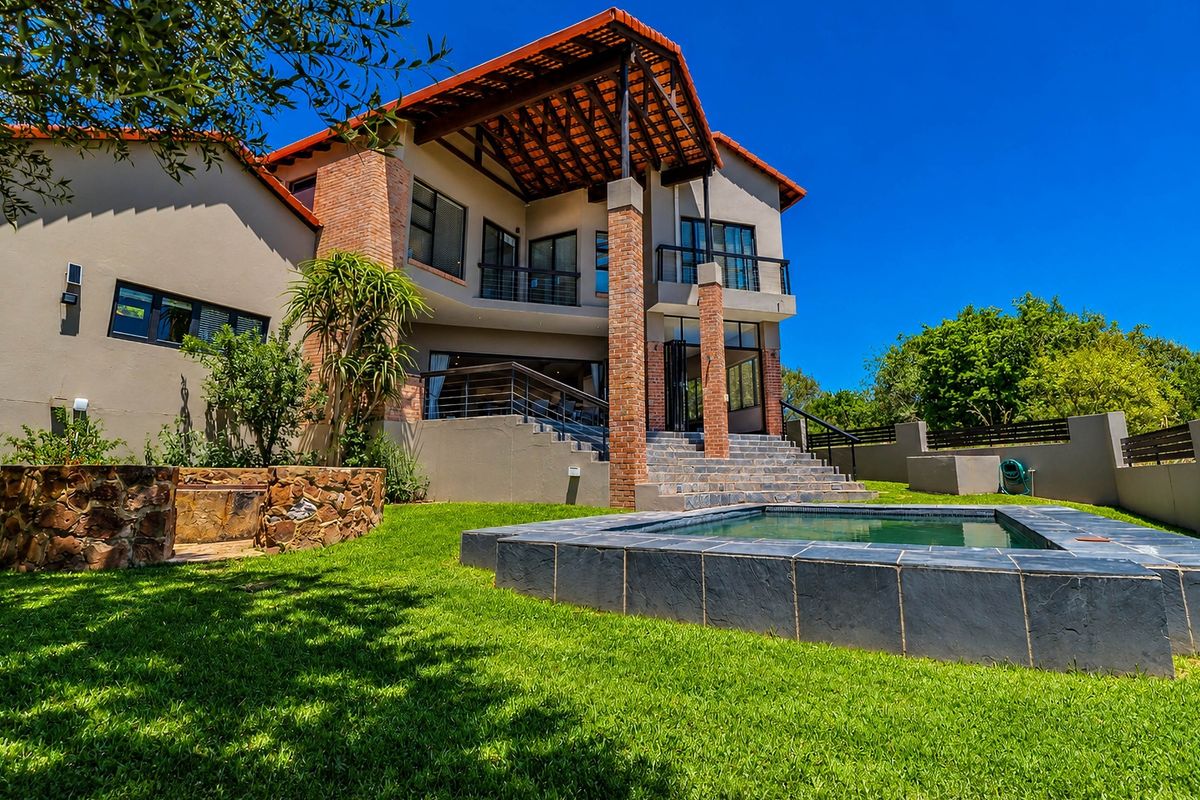 Rear view of a multi-level house featuring a swimming pool, stone retaining wall, covered patio, and balcony with brick architectural details.