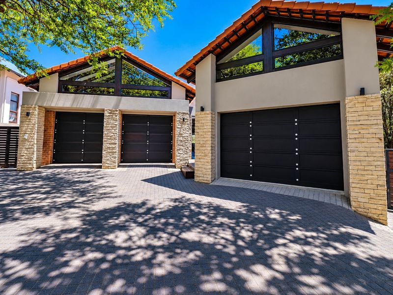 A modern triple garage featuring dark panelled doors, stone-clad pillars, and distinctive triangular clerestory windows, set against a neatly paved driveway.