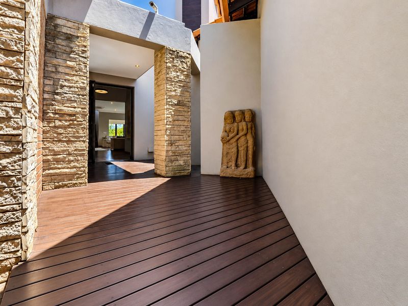 A modern, covered outdoor patio featuring high-quality timber decking and elegant stone-clad pillars, creating a seamless transition to the interior living space.