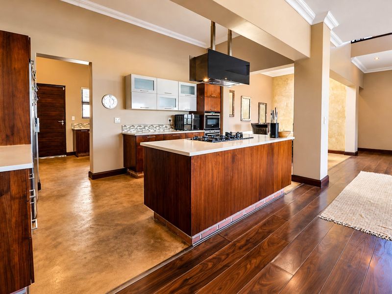 Modern open-plan kitchen featuring a central island with gas hob, built-in oven, sleek wooden cabinetry, and a combination of polished concrete and hardwood flooring.