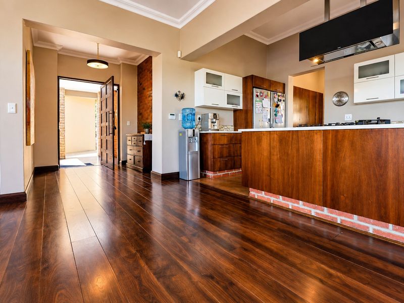 Spacious open-plan kitchen and living area featuring rich laminate flooring, a central kitchen island, and an attractive exposed brick accent wall.