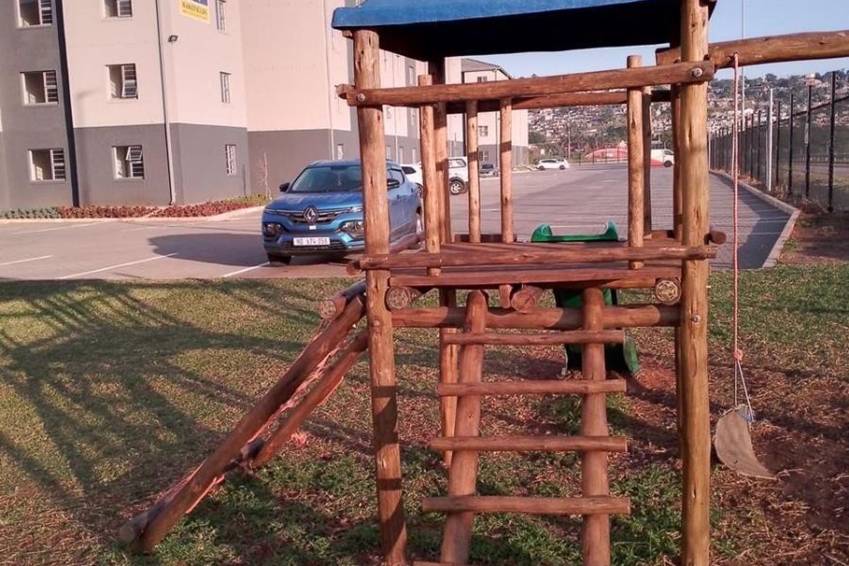 Exterior view of the apartment complex grounds featuring a wooden playground structure and paved parking area.