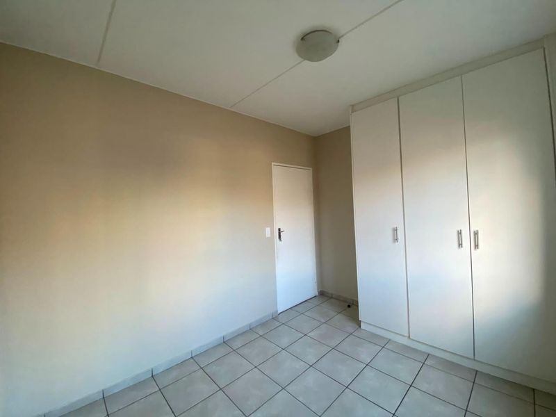 An empty bedroom featuring neutral wall paint, tiled flooring, and white built-in cupboards providing ample storage space.