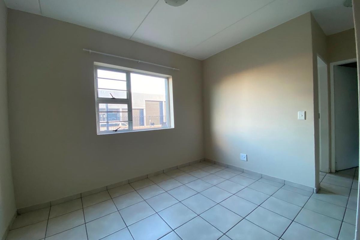 A clean, empty bedroom featuring neutral tiled flooring and a large aluminium window, providing a blank canvas for personalization.