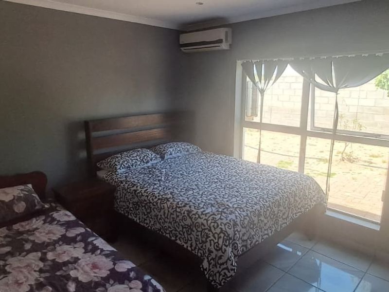 A functional bedroom featuring tiled flooring, a large window for natural light, and a wall-mounted air conditioning unit.