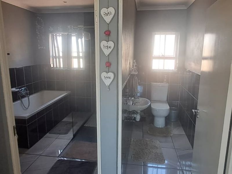 A functional bathroom featuring a built-in bathtub, pedestal basin, and toilet with tiled finishes throughout.