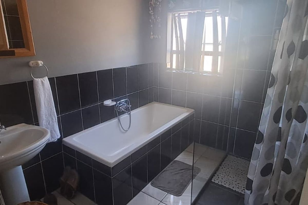 A functional bathroom featuring a pedestal basin, a built-in bathtub with black wall tiling, and tiled flooring.