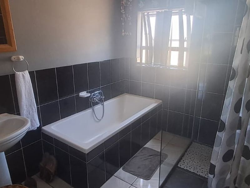A functional bathroom featuring a pedestal basin, a built-in bathtub with black wall tiling, and tiled flooring.