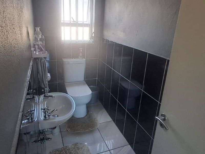 A compact bathroom featuring a pedestal basin, toilet, and contrasting black wall tiles with light floor tiles.