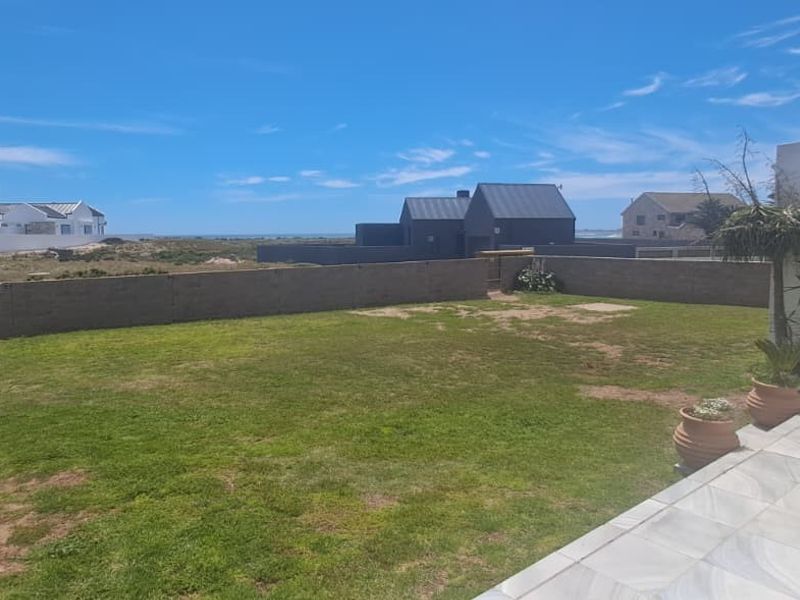 A rear garden featuring a tiled patio area, lawn, and boundary wall with views of the surrounding neighborhood.
