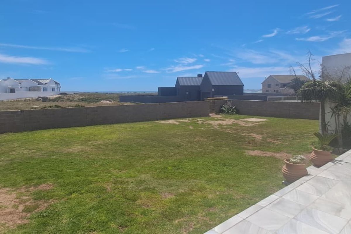 A rear garden featuring a tiled patio area, lawn, and boundary wall with views of the surrounding neighborhood.