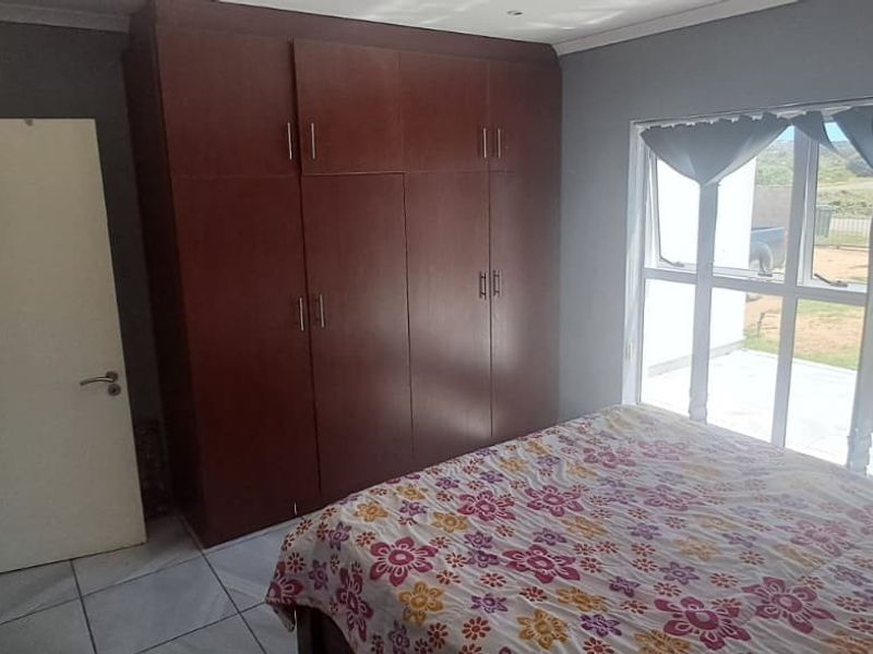A bedroom featuring built-in wooden cupboards, tiled flooring, and a large window providing natural light and exterior views.