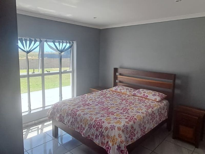 A bedroom featuring tiled flooring, neutral grey walls, and a large window providing natural light and garden views.
