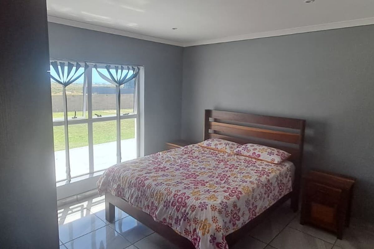 A bedroom featuring tiled flooring, neutral grey walls, and a large window providing natural light and garden views.