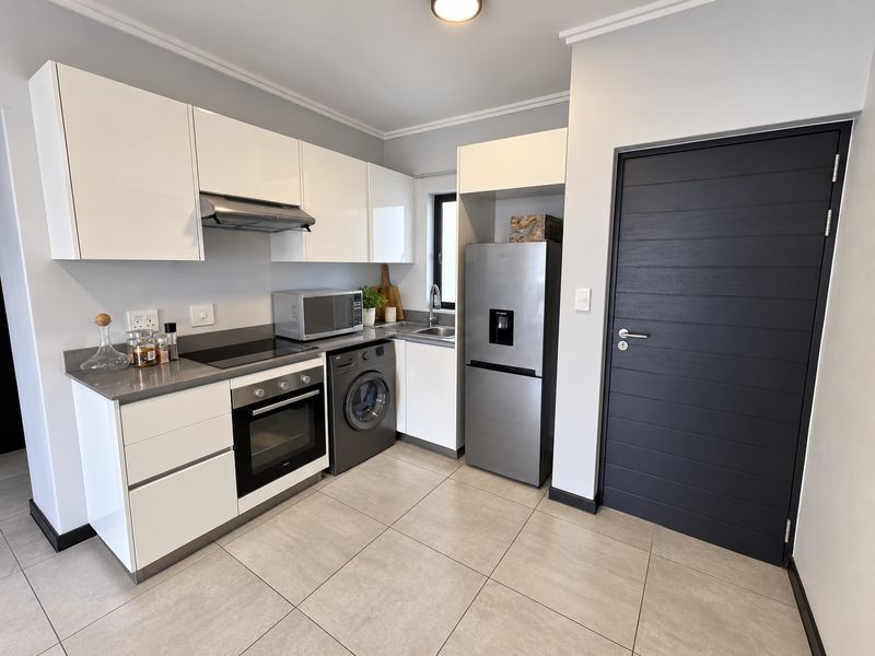 A modern, well-maintained kitchen featuring white cabinetry, stone countertops, integrated appliances, and sleek tiled flooring, complemented by a contemporary dark-toned internal door.