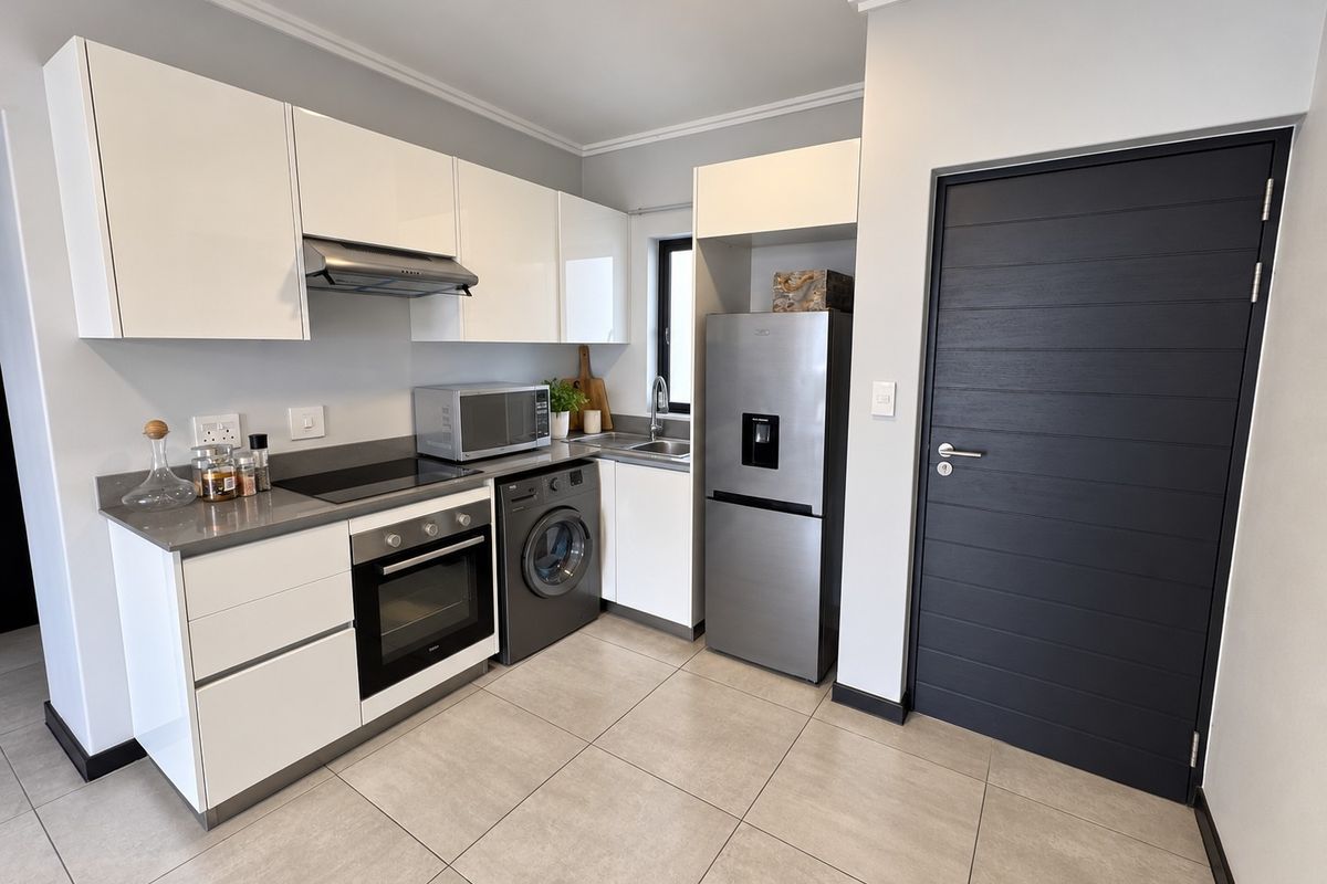 A modern, well-maintained kitchen featuring white cabinetry, stone countertops, integrated appliances, and sleek tiled flooring, complemented by a contemporary dark-toned internal door.