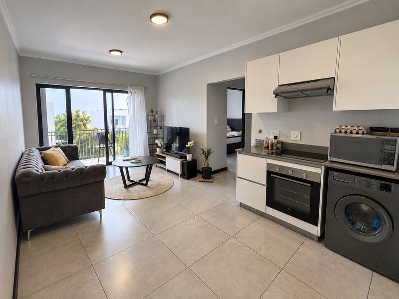 Modern open-plan living area featuring a compact kitchen with built-in appliances, tiled flooring, and direct access to a private balcony.
