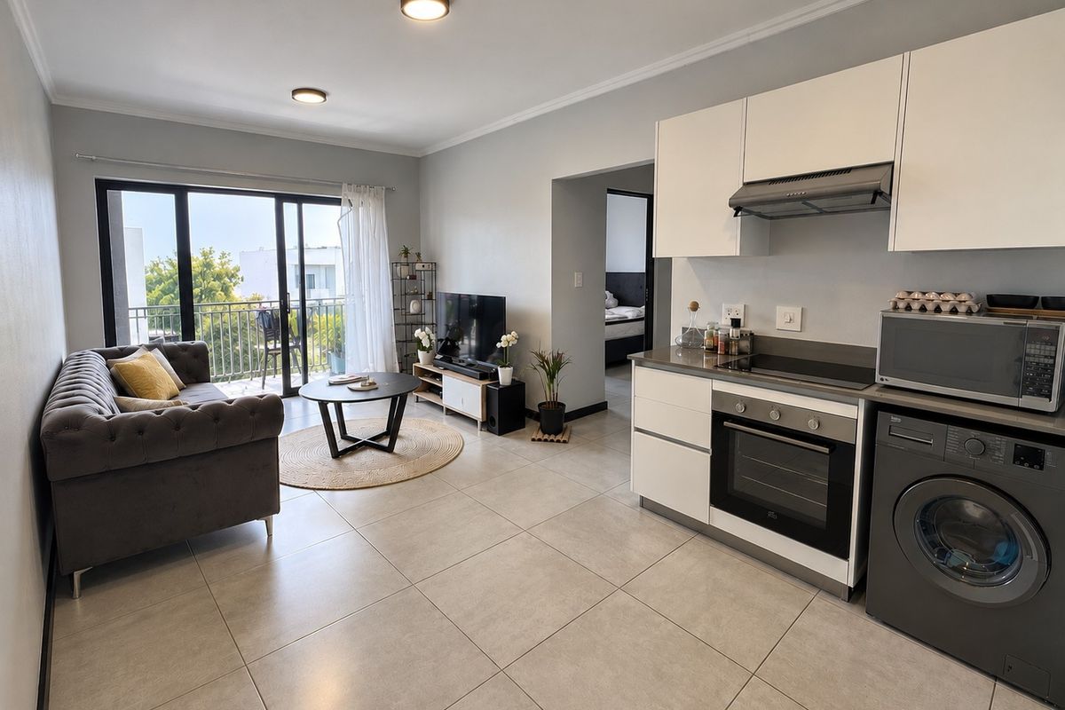 Modern open-plan living area featuring a compact kitchen with built-in appliances, tiled flooring, and direct access to a private balcony.