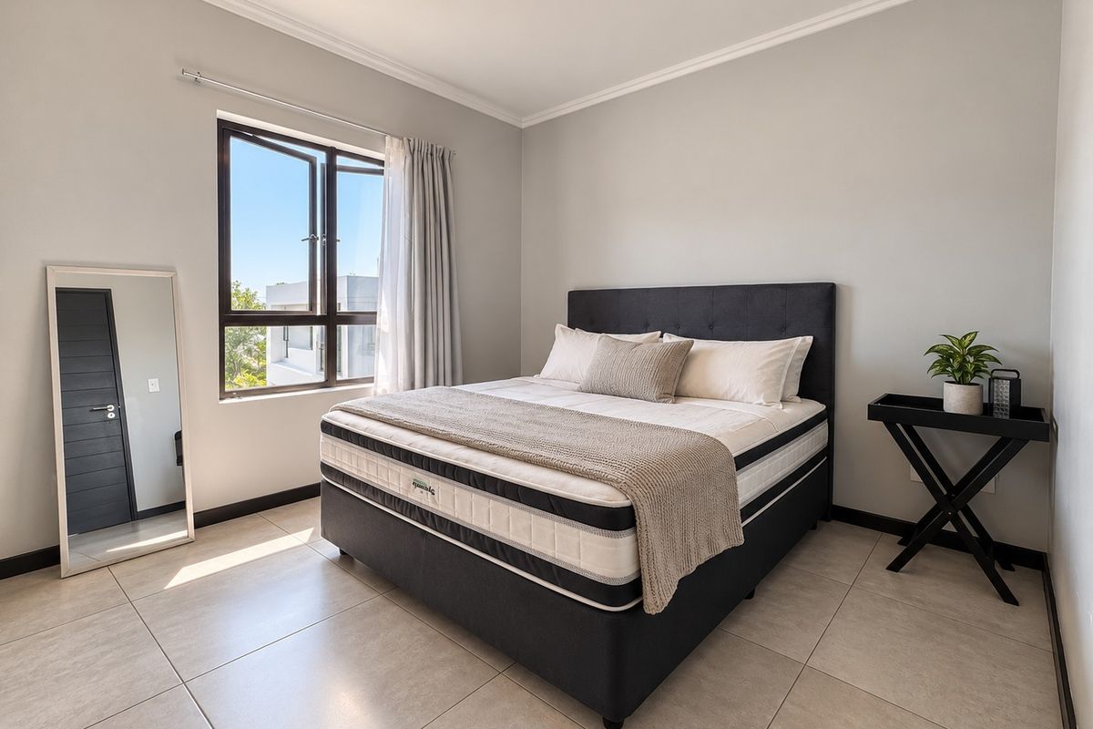 A bright and well-maintained bedroom featuring neutral tiled flooring, clean wall finishes, and a large casement window allowing for ample natural light.