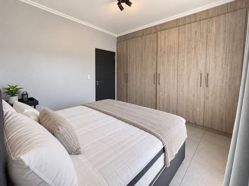 A well-maintained bedroom featuring modern wood-finish built-in cupboards, neutral tiled flooring, and a contemporary ceiling spotlight.