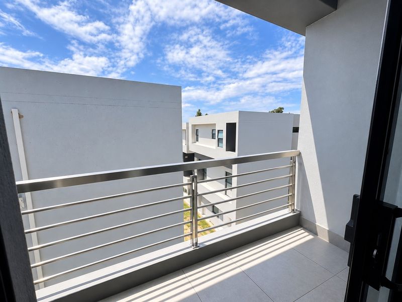 A modern, clean balcony featuring a stainless steel balustrade and neutral floor tiling, offering an open view of the surrounding apartment complex.