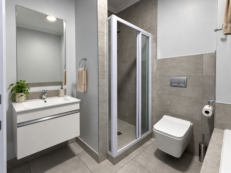 Modern bathroom featuring a wall-mounted vanity with integrated basin, a glass-enclosed shower, and a sleek wall-hung toilet with neutral tiled finishes.