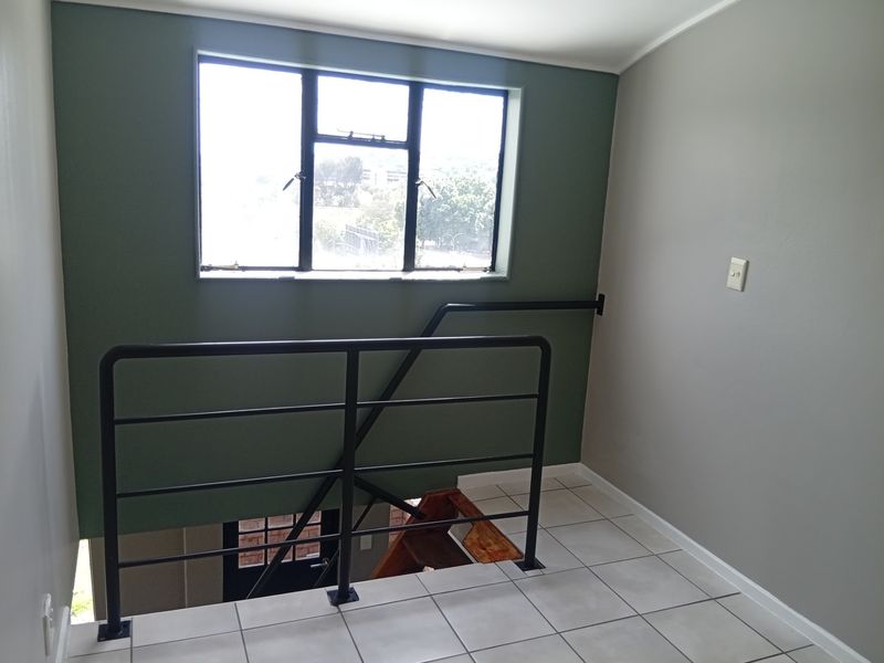 A bright, empty landing area featuring tiled flooring, a metal safety balustrade, and a window overlooking the exterior.