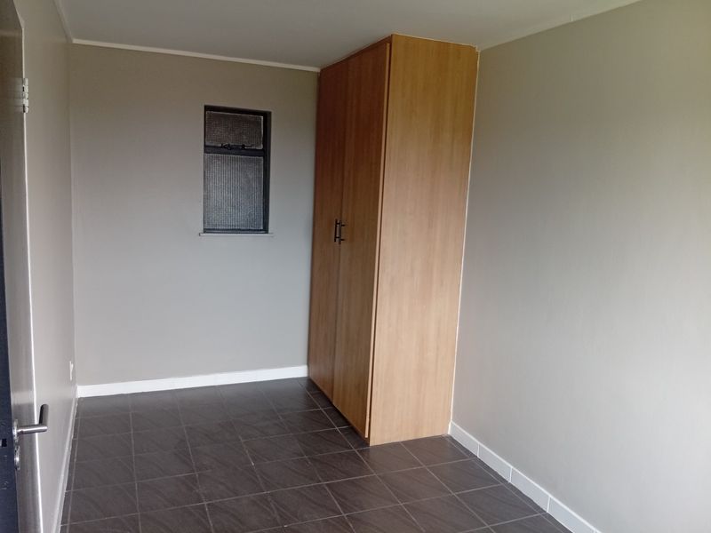 A clean, empty bedroom featuring neutral wall tones, dark tiled flooring, and a built-in wooden wardrobe.