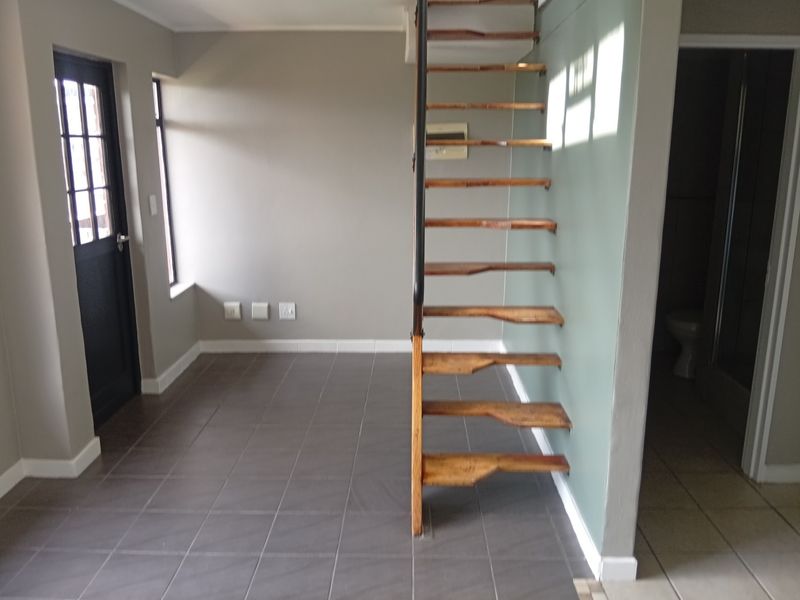 An open-plan living area featuring modern tiled flooring and a distinctive open-tread timber staircase leading to an upper level.