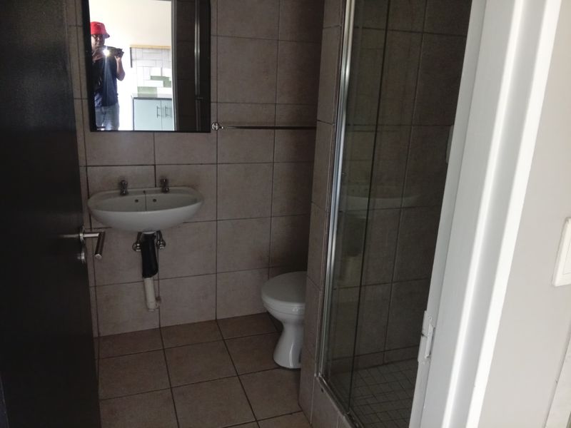 A functional bathroom featuring a wall-mounted basin, toilet, and a glass-enclosed shower with neutral wall and floor tiling.