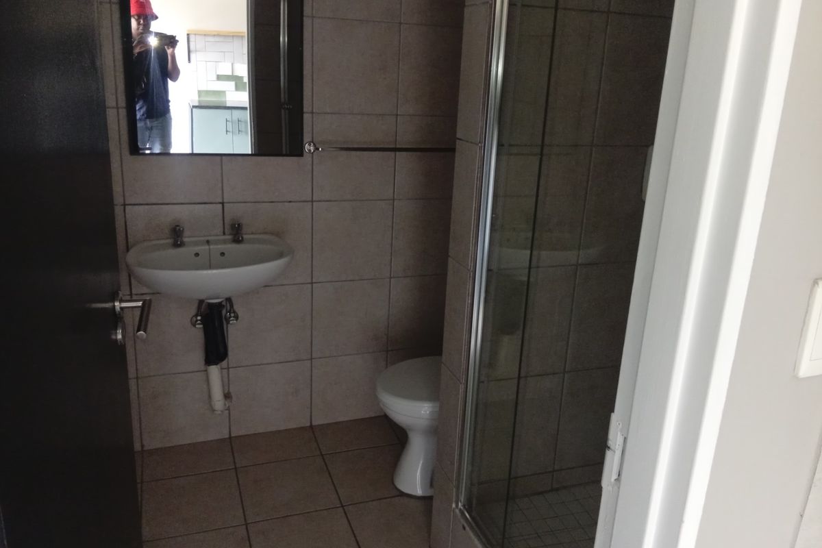 A functional bathroom featuring a wall-mounted basin, toilet, and a glass-enclosed shower with neutral wall and floor tiling.