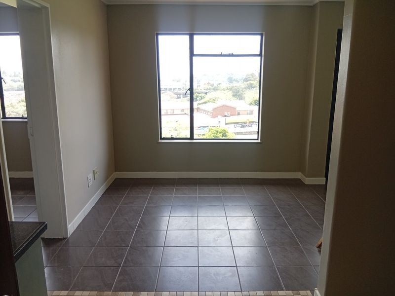 An empty living area featuring dark tiled flooring and a large window providing natural light and an urban view.