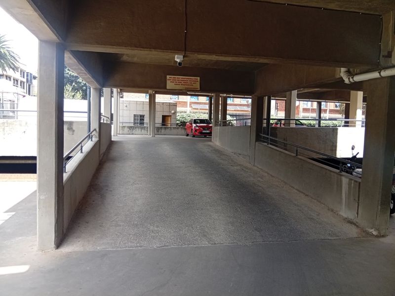 A covered concrete parking ramp with metal safety railings and structural pillars, providing access to the apartment complex parking area.