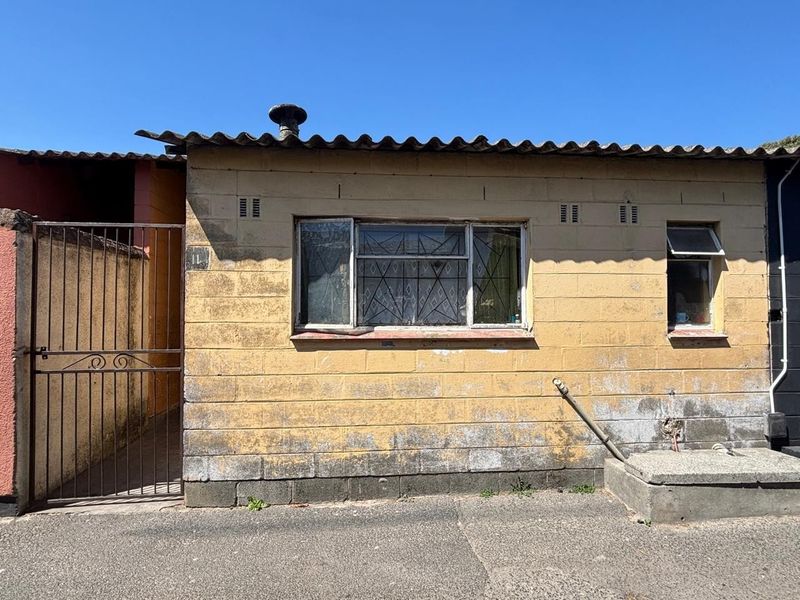 Front exterior view of a residential unit featuring a corrugated roof, security gate, and weathered concrete block walls requiring maintenance.
