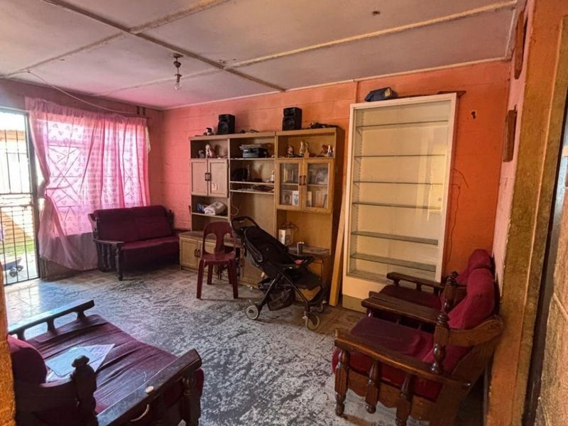 A living room area featuring tiled flooring, a security gate, and exposed ceiling panels, requiring cosmetic updates to improve the overall condition.