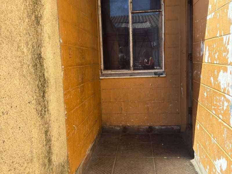 A small, covered outdoor balcony area featuring masonry walls and tiled flooring, currently requiring maintenance and cosmetic updates to improve its overall condition.