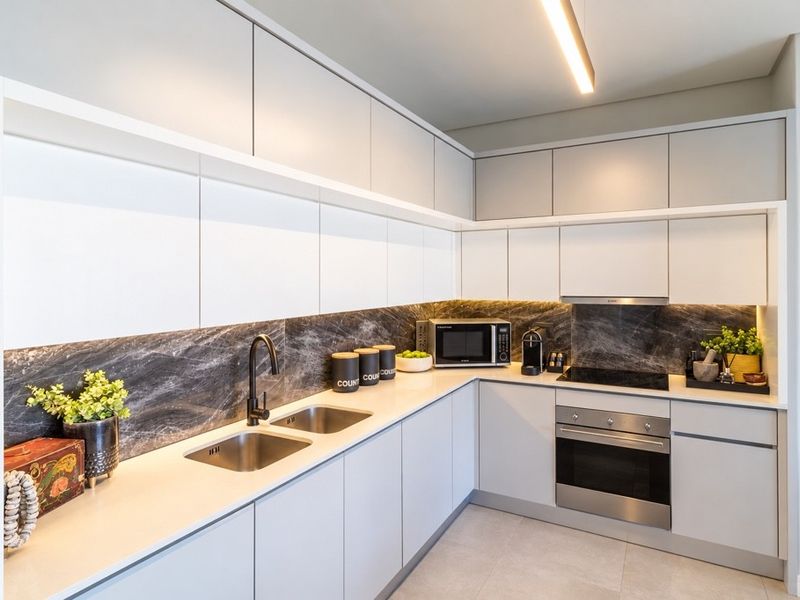 Modern kitchen featuring sleek handleless cabinetry, stone countertops, dark marble-effect splashback, and integrated stainless steel appliances.