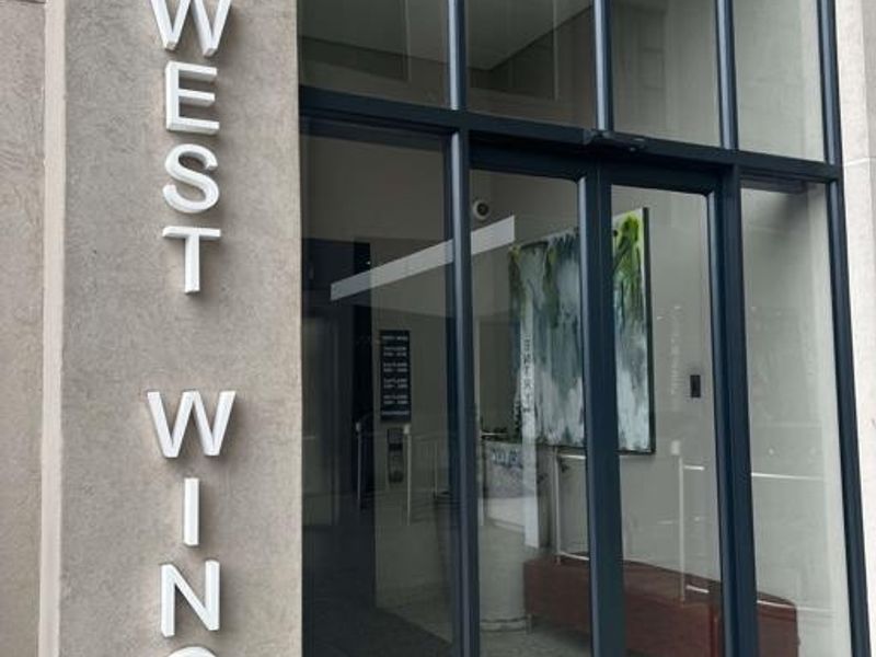 Modern building entrance featuring a glass facade with aluminium framing and stone cladding, clearly marked as the West Wing.