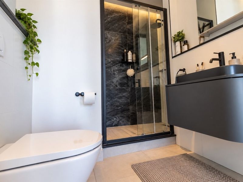 Modern bathroom featuring a wall-hung toilet, floating vanity with integrated basin, and a sleek walk-in shower with black frame and dark marble-effect tiling.