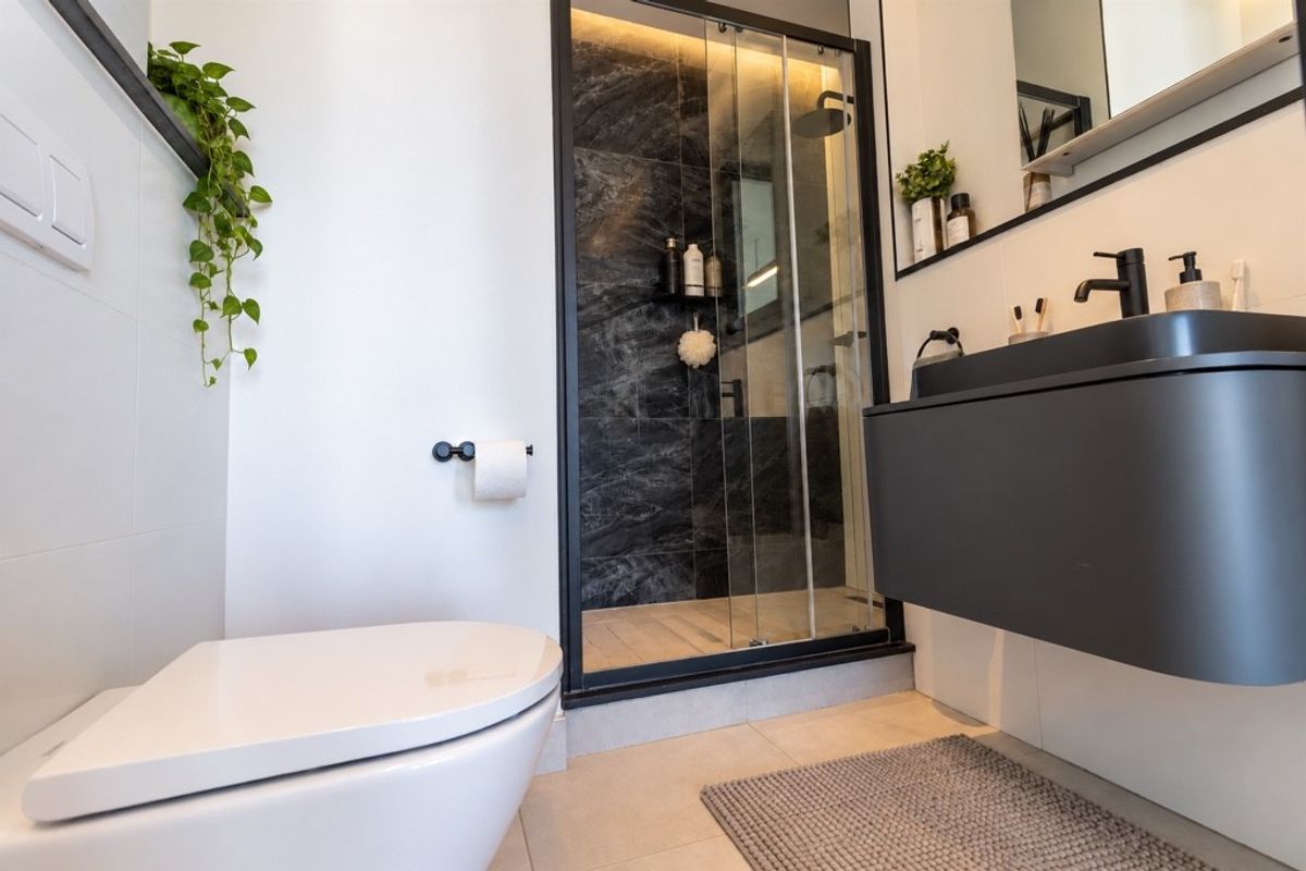 Modern bathroom featuring a wall-hung toilet, floating vanity with integrated basin, and a sleek walk-in shower with black frame and dark marble-effect tiling.