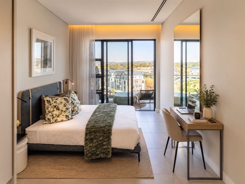 Modern penthouse bedroom featuring tiled floors, recessed lighting, and large sliding glass doors opening onto a private balcony with scenic views.