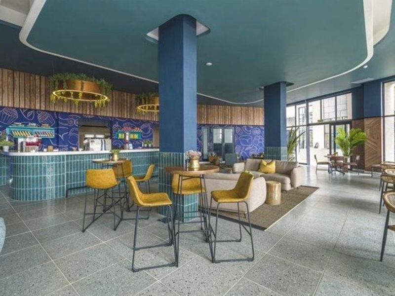 A modern, well-appointed clubhouse area featuring a tiled bar counter, structural columns, and expansive floor-to-ceiling windows with contemporary finishes.