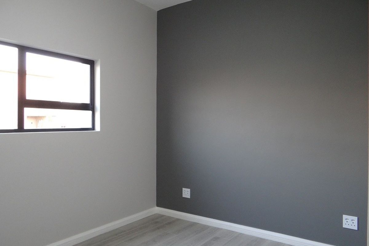 A clean, empty bedroom featuring modern grey laminate flooring, a dark grey accent wall, and a contemporary aluminium-framed window.
