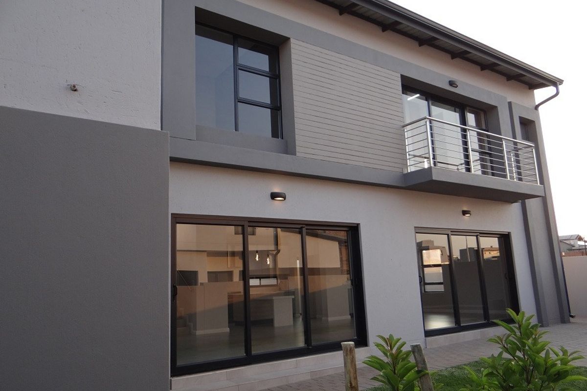 Modern two-story rear facade featuring large sliding glass doors, a private balcony with stainless steel railing, and paved patio area.