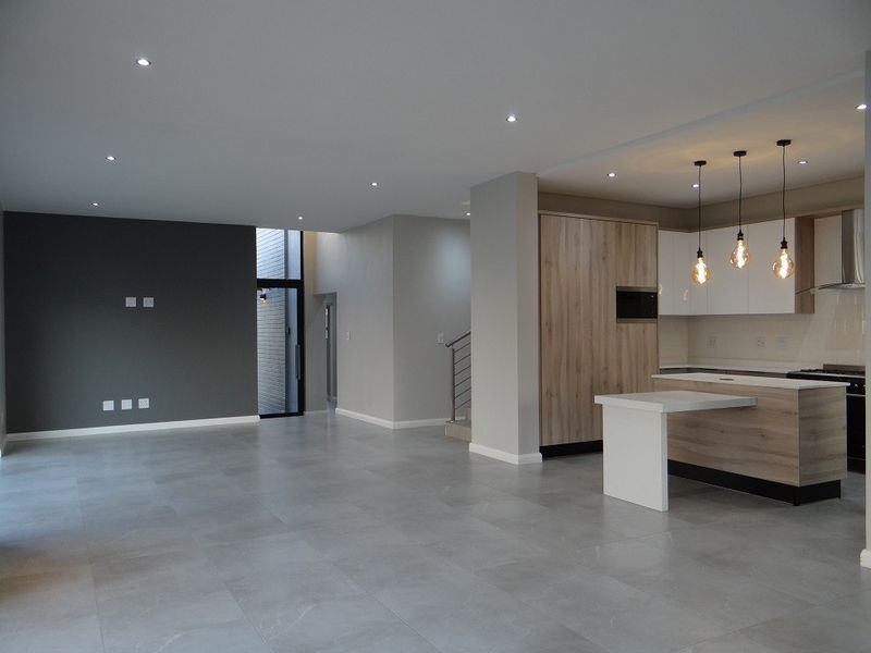 Spacious open-plan living and kitchen area featuring modern cabinetry, a central island, recessed lighting, and neutral tiled flooring throughout.
